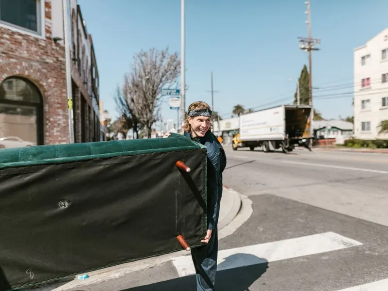 Removal man carrying a green sofa across the road to a waiting van