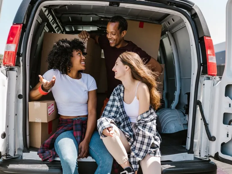Two students sitting in the back of a loaded van with their boxes